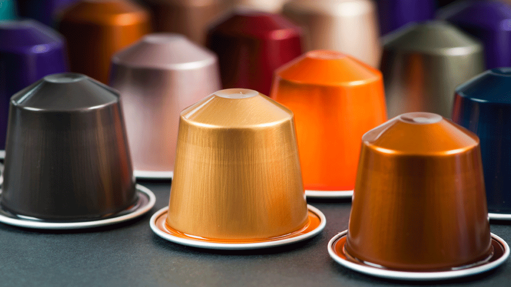 Main sélectionnant une dosette café parmi plusieurs références sur un plan de travail