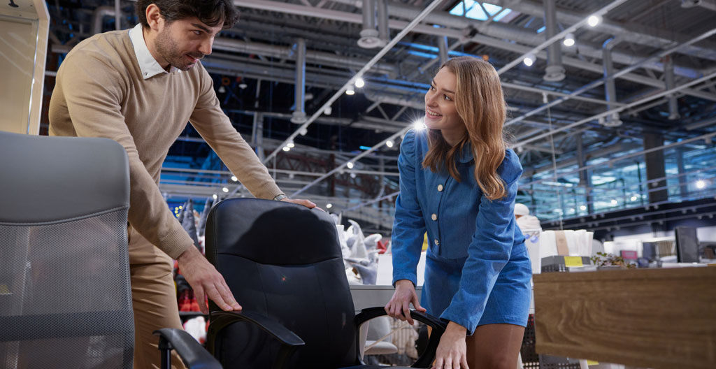 Consultant en ergonomie expliquant le fonctionnement d'un siège à un responsable achats dans un showroom
