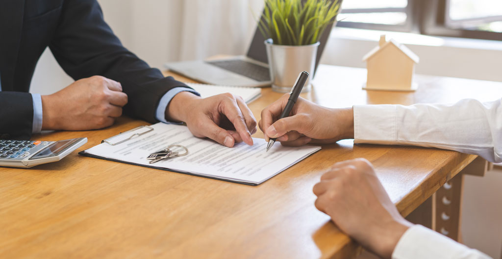 Gros plan sur des mains feuilletant un contrat de bail commercial aux pages légèrement jaunies, avec un stylo posé à côté sur une table en bois