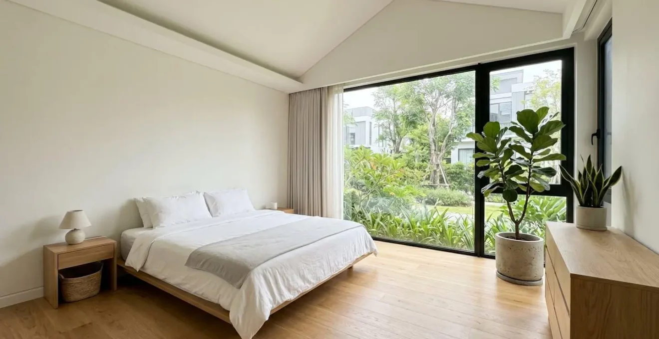 Chambre contemporaine vide et lumineuse avec lit fait en linge blanc, grande fenêtre ouverte laissant entrer la lumière naturelle et plantes vertes d'intérieur