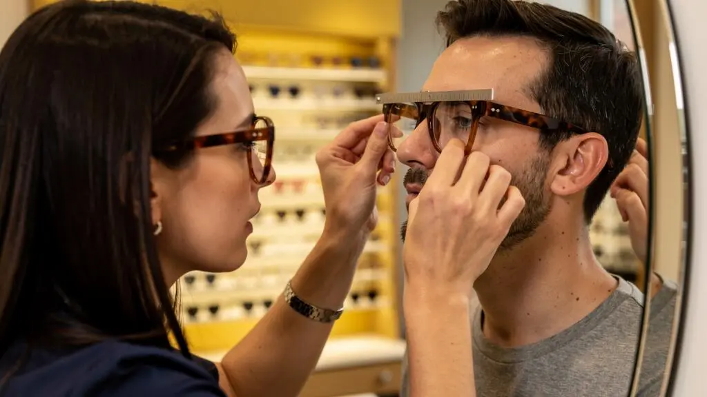 Un opticien mesure l'écart pupillaire d'un client essayant une monture ambrée.